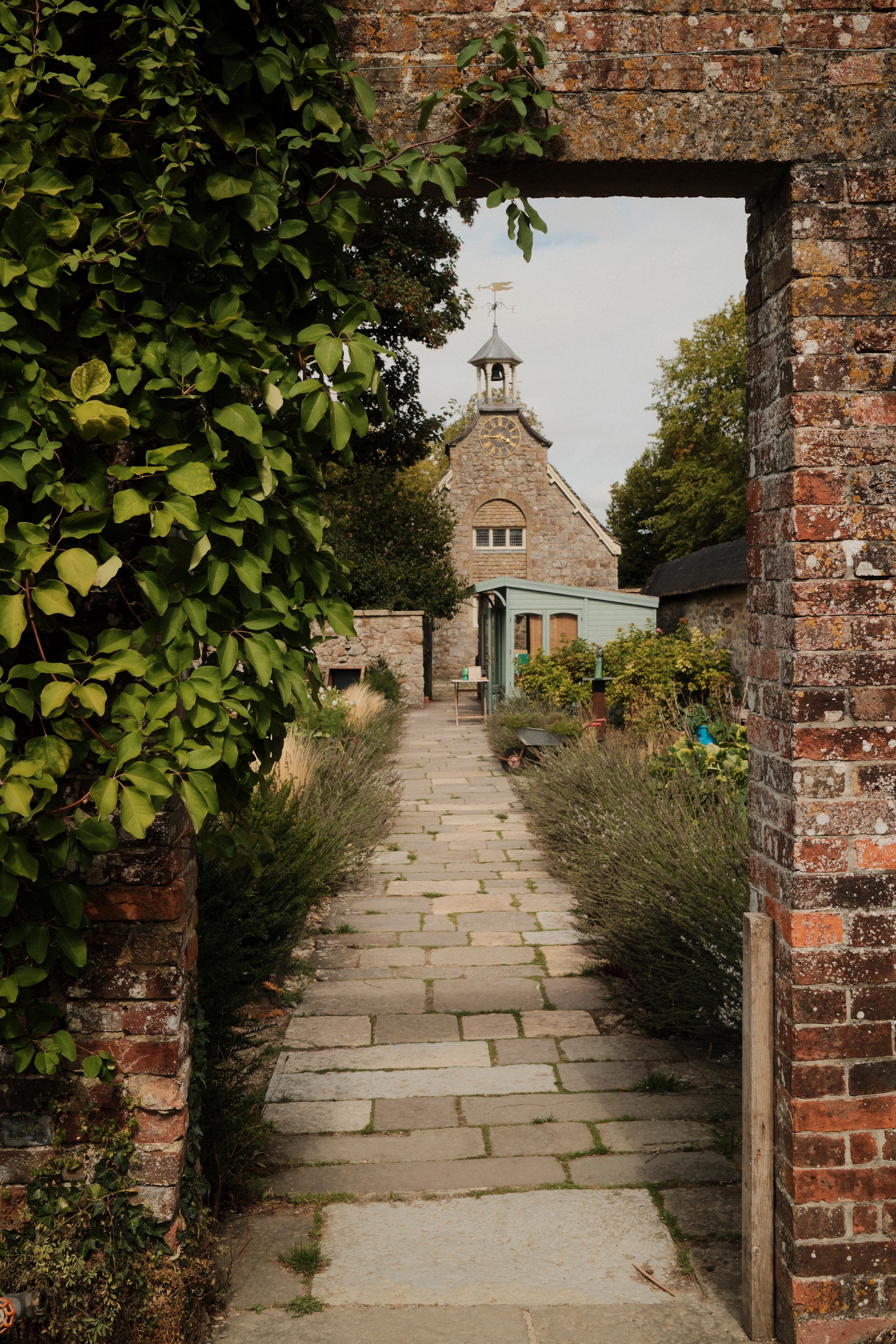 A leafy brick opening frames a path and distant building